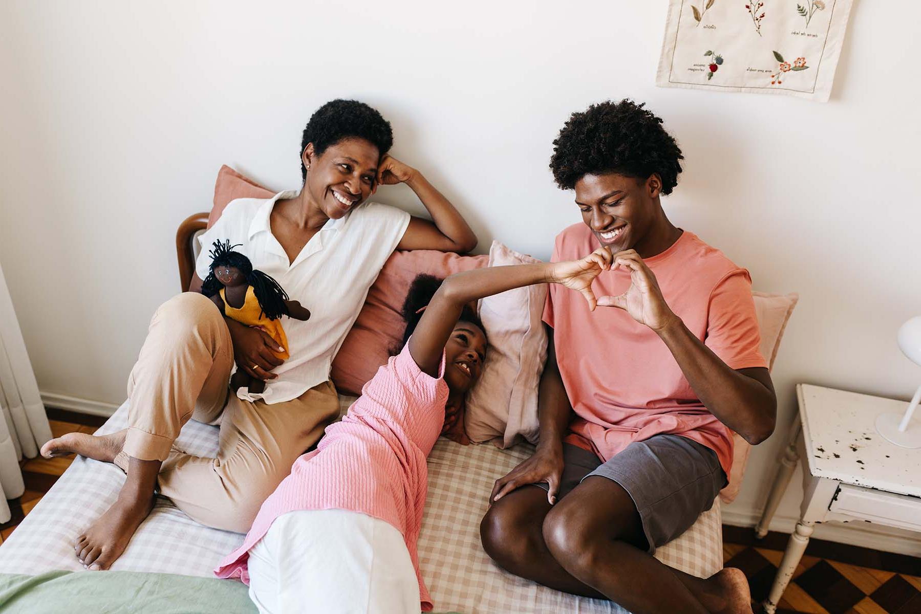 A family forms a heart shape with their hands, smiling on a bed